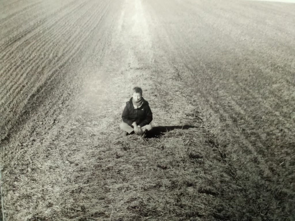Kobieta siedzi na ziemi. Dookoła pole.