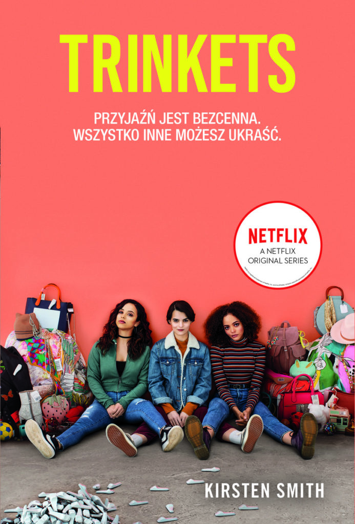 Na okładce trzy dziewczyny siedzące na tle łososiowej ściany. Obok plecaki, torby, ubrania. Logo Netflix.