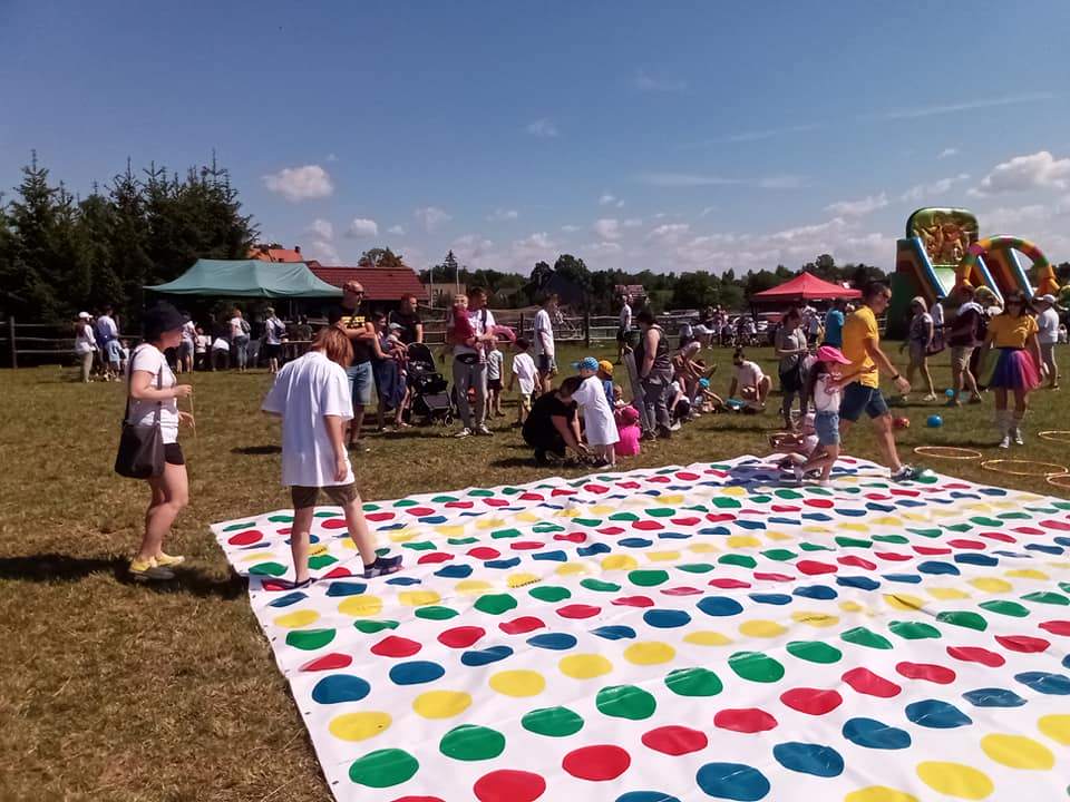 Sportowa sobota w Mikoszowie. Dzieci, młodzież i dorośli stoją na trawie przy grze "Twister"w rozmiarze XL.