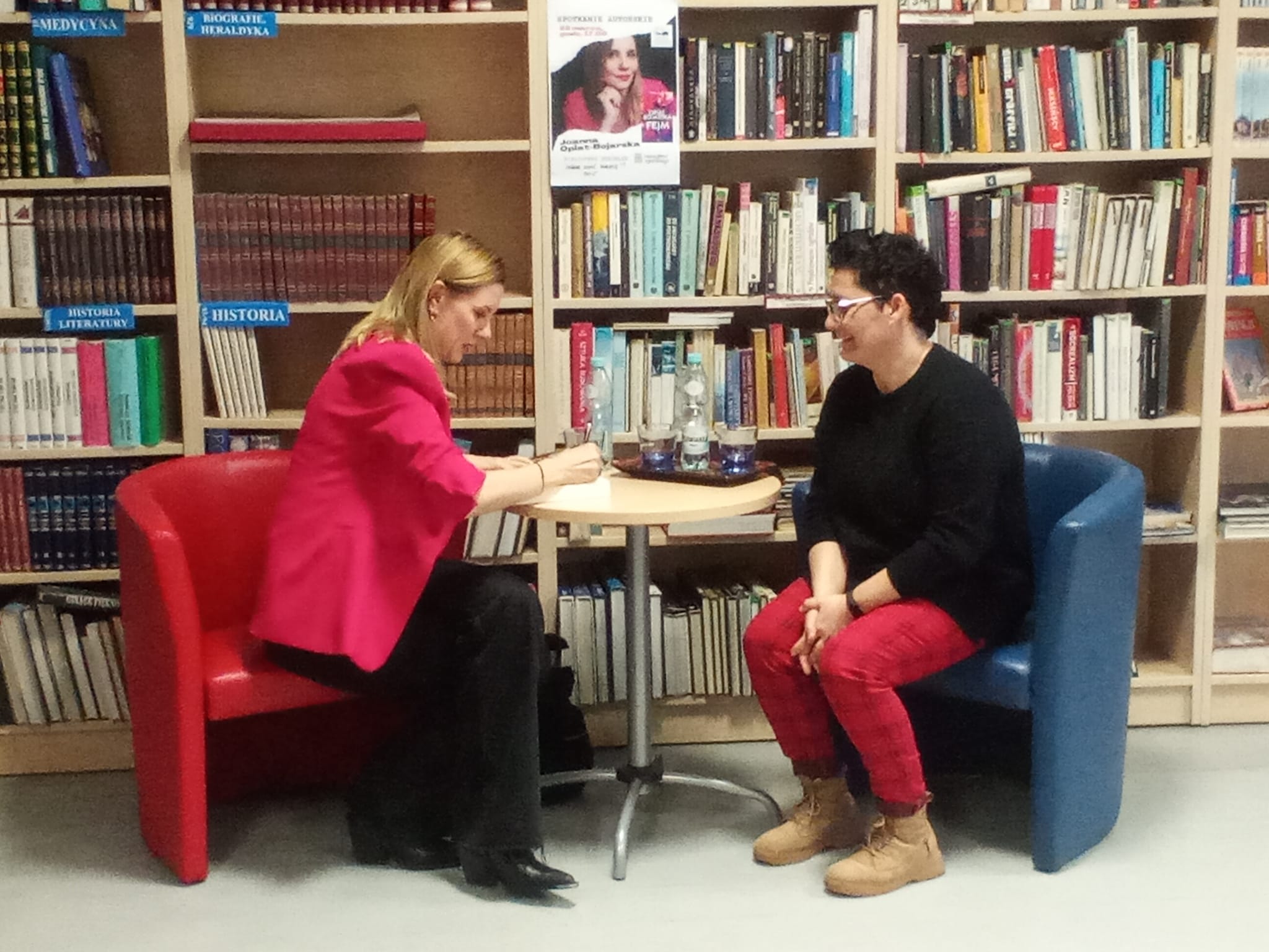Czytelnia biblioteki, spotkanie autorskie z Joanną Opiat-Bojarską, dwie kobiety siedzą w fotelach i rozmawiają