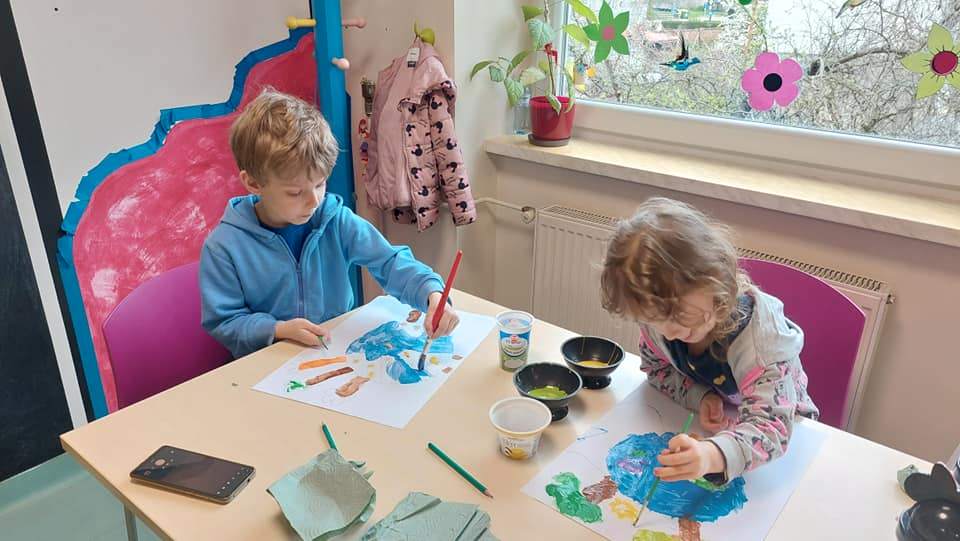 Czytelnia dla dzieci. Dwoje dzieci siedzi przy stoliku i maluje farbami plakat o Ziemi