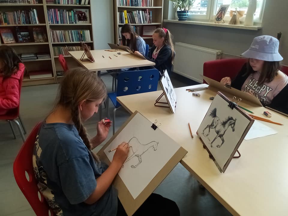 Czytelnia biblioteki pięć dziewczynek siedzi przy stole rysując konia