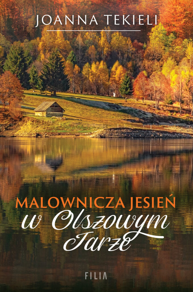 Na okładce jesienny krajobraz: mały drewniany domek przy jeziorze, w tle mnóstwo drzew w jesiennych kolorach
