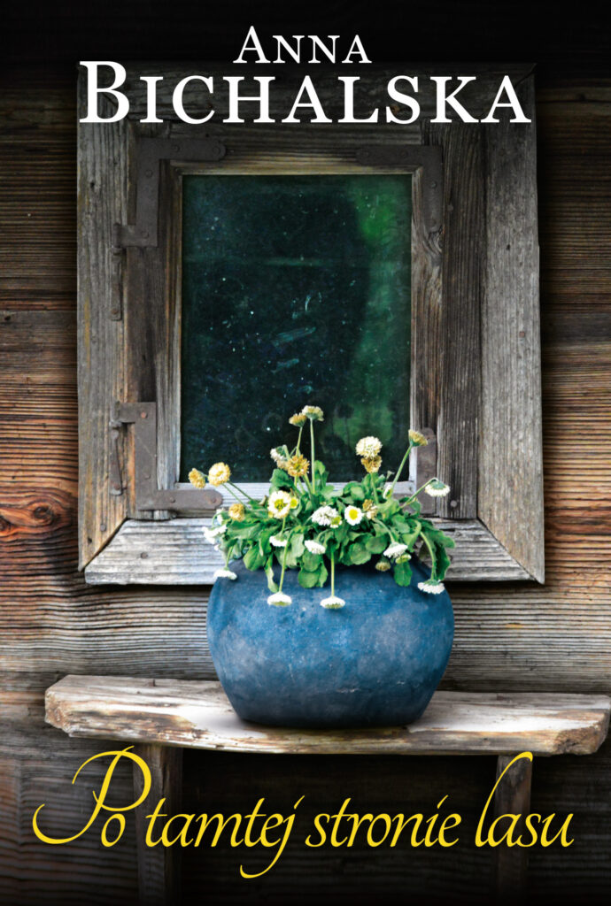 Na okładce niebieska donica ze stokrotkami na drewnianej półce przy małym oknie drewnianej ściany